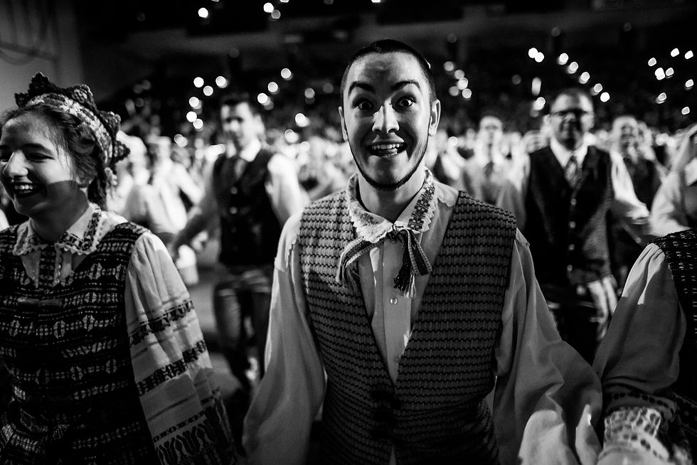 Black-and-white photograph of a man in an embroidered vest moving beside other performers beneath arena lights.