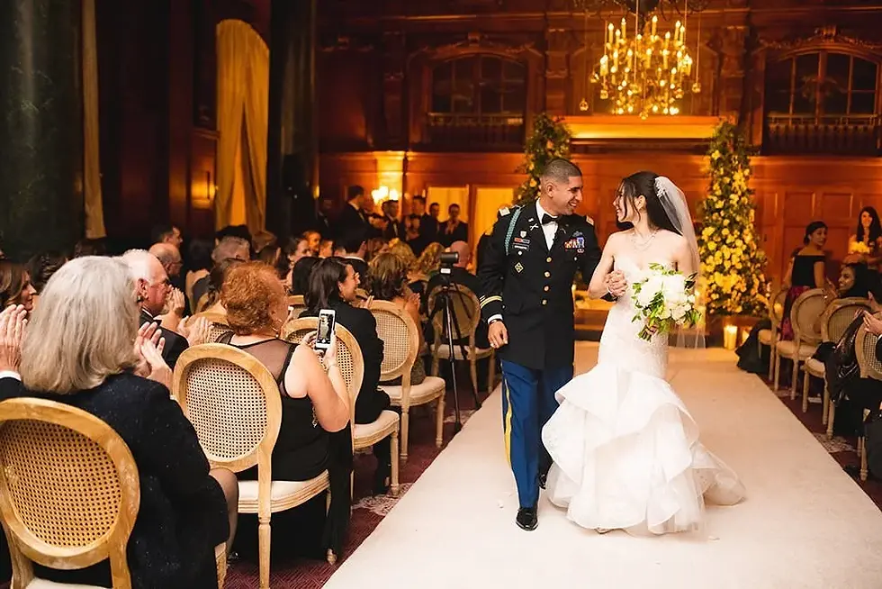 Bride and uniformed groom walking down a ceremony aisle.