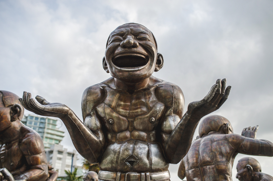 A bronze sculpture of a laughing figure with both palms raised, with other figures behind it.