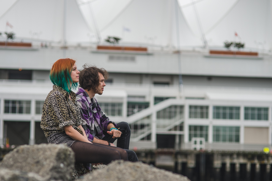 Two people seated on rocks with a large white waterfront building behind them.