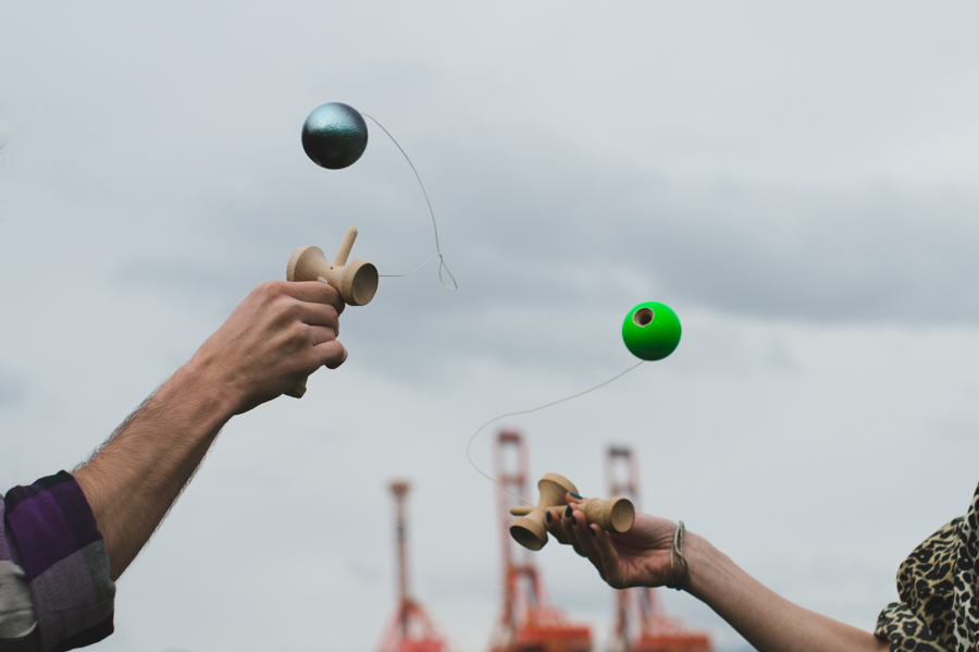 Two hands holding wooden cup toys as attached colored balls hang in the air.