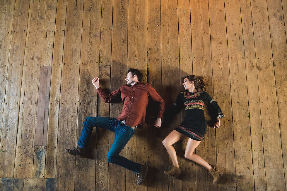 Overhead view of a couple lying playfully on a wooden floor.