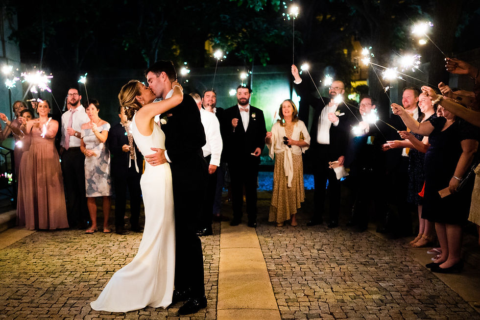 Bride and groom kissing as guests hold sparklers around them.