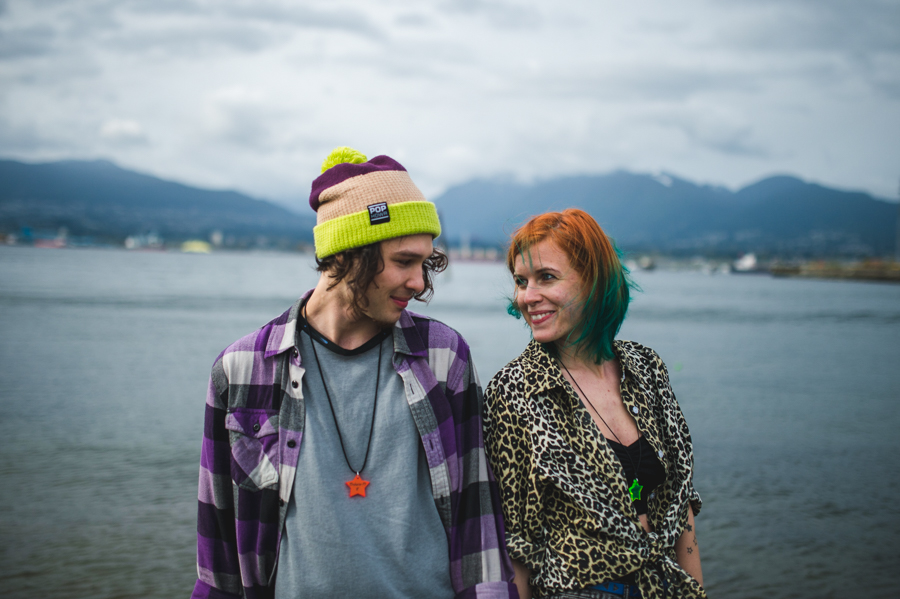 Two people looking at one another beside the water, with mountains in the distance.