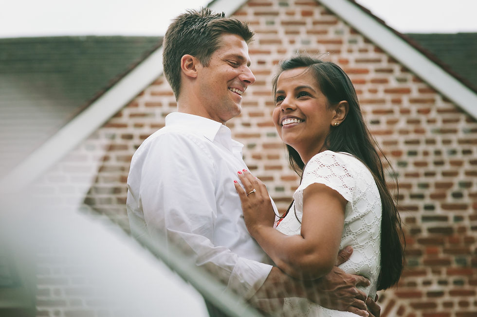 Man and woman embracing in front of a brick gable, with faint overlapping shapes across the foreground