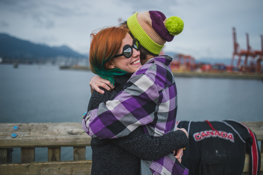Two people embracing beside a waterfront railing, with cranes across the water.