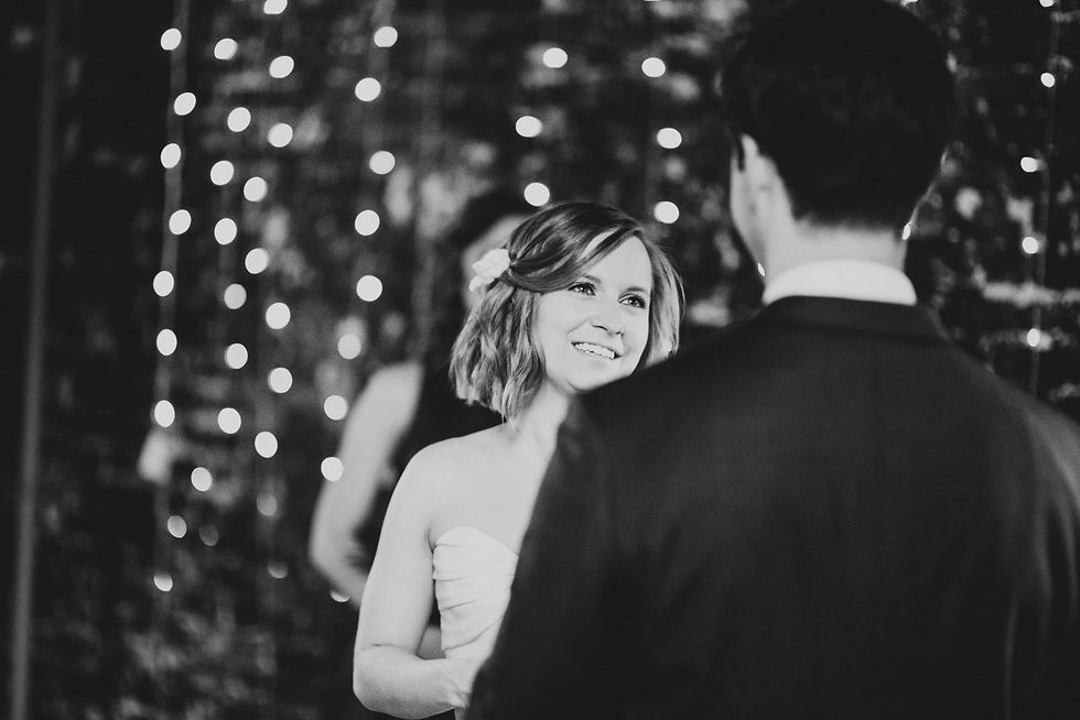 Bride smiles at the groom beneath string lights