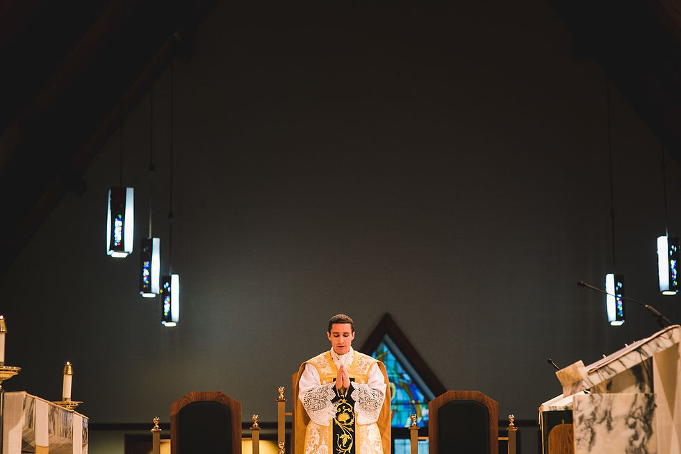 Cleric in white and gold vestments before an altar beneath a high timber ceiling and hanging lights