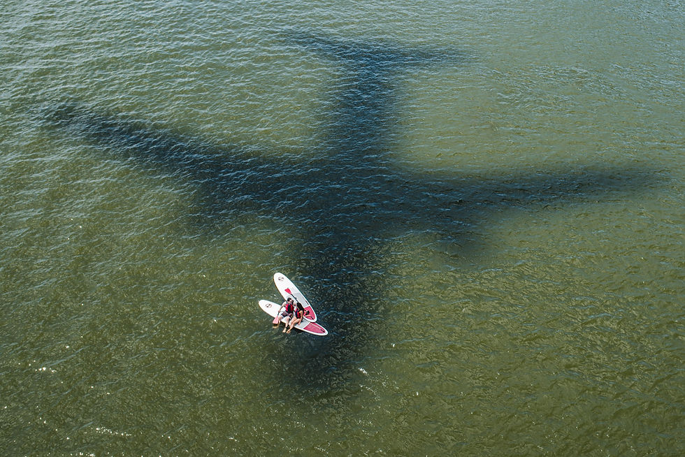 Aerial view of a couple on a paddleboard beneath an airplane shadow.