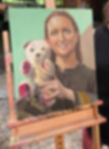 Portrait painting on an easel of a smiling woman with shoulder-length reddish-brown hair, wearing a dark uniform with gold epaulettes, holding a signed teddy bear with tartan-patched paws against a mint-green background.
