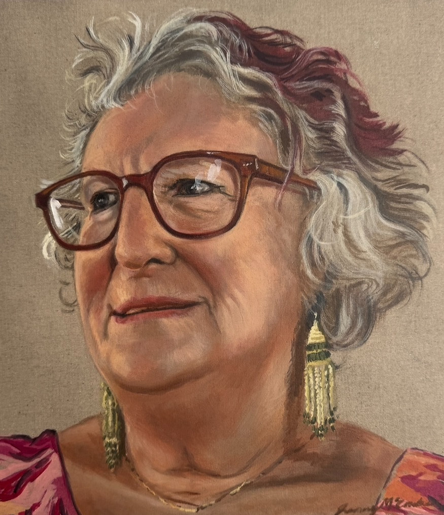 Framed portrait painting of a smiling older woman with curly grey and maroon-streaked hair, glasses, tassel earrings, and a colorful patterned top.
