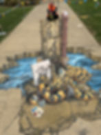 3D pavement art of a large blue-ringed octopus painting at an easel beside a wooden post and pipe, with water flowing around a cracked pavement illusion; a woman sits atop the post. Signed "Jenny McCracken" and dated 2026.