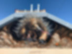 Mural of an echidna and its baby (puggle) painted beneath the eaves of a building, tongue extended toward the ground, against a blue sky.