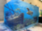 Mural inside a warehouse showing an underwater scene with a sunken shipwreck, sea turtles, coral, and a treasure chest, wrapping around the corner of two walls.