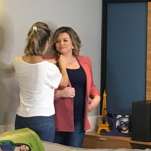 A consultora Mônica Deitos faz pequenos ajustes na dobra da gola do blazer Carolina Rocha, sócia da Palavra Bordada. As duas estão em pé e olham uma para a outra. 