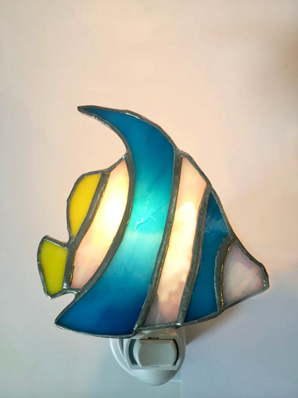 Stained glass fish nightlight plugged in and lit against the wall