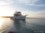 White trawler anchored on calm water at sunset.