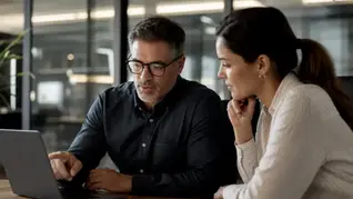 A manager reviewing and approving a deal on screen with a colleague in a modern office, slate-gray with warm amber accents.