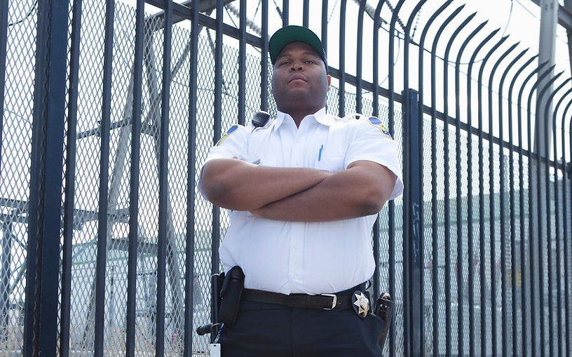 Security guard standing with arms crossed near fence