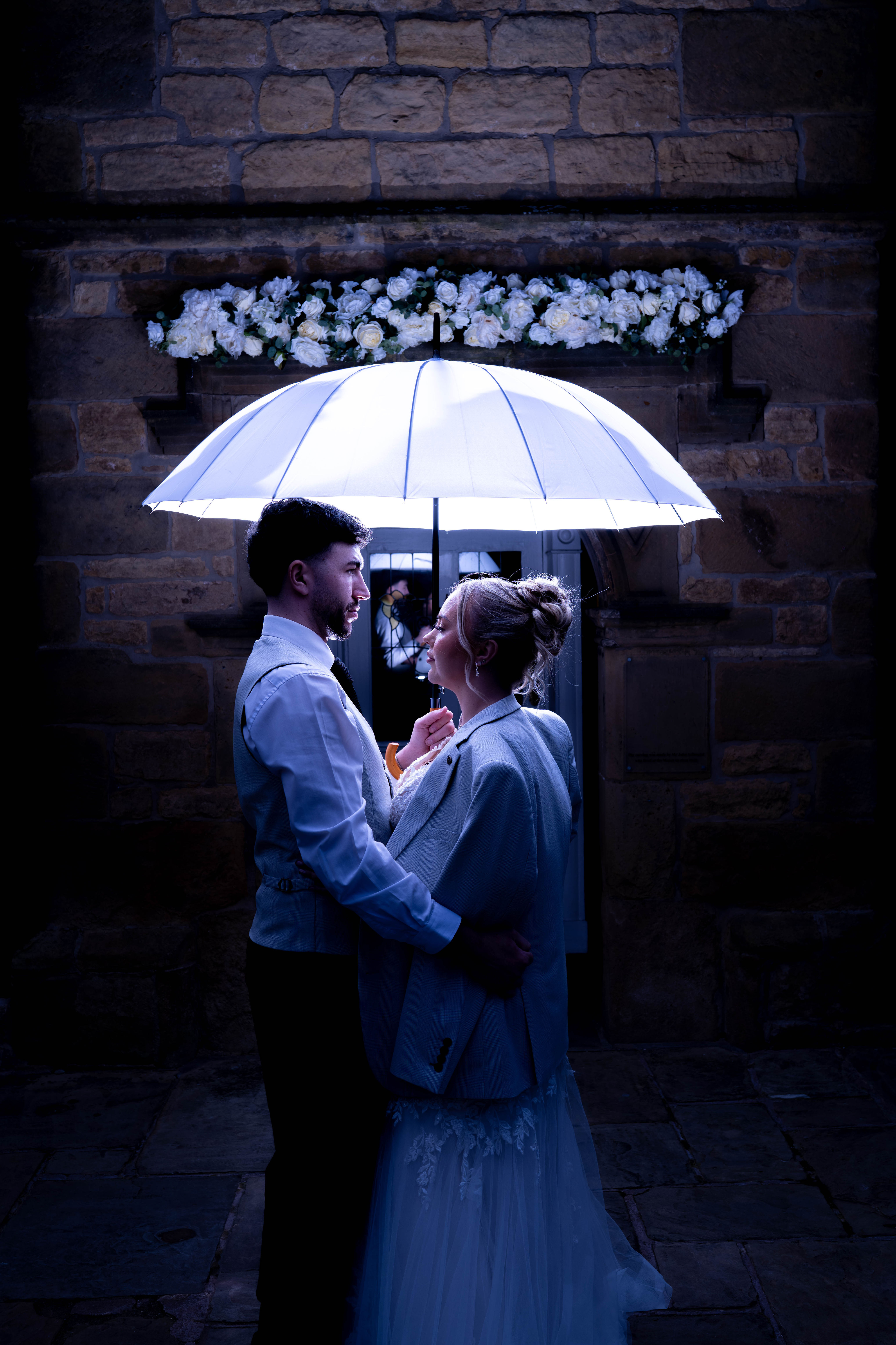 A bride and groom holding an illuminated umbrella 