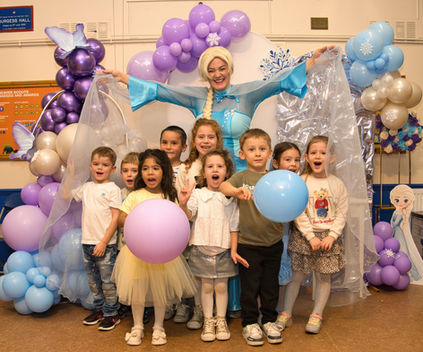 Children posing with entertainer dressed as ice princess surrounded by purple and blue balloons