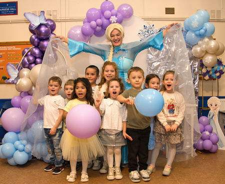 A group of smiling children stands with a performer in an ice-themed costume