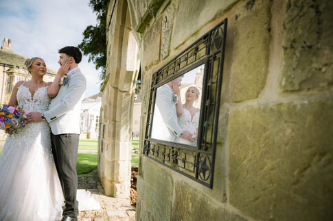 Bride and groom posing beside stone wall with mirror reflection during outdoor wedding shoot