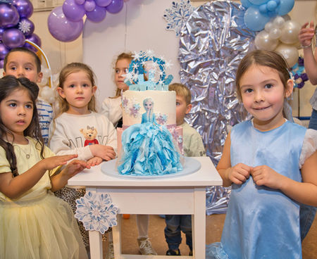 Children at a birthday party gather around a cake decorated with a blue princess