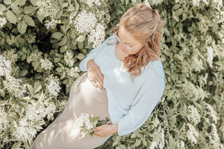 Schwangere Frau hält ihren Bauch und weiße Blüten im Freien.