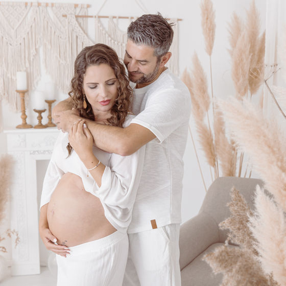 Paar bei Babybauch-Shooting, Mann umarmt schwangere Frau