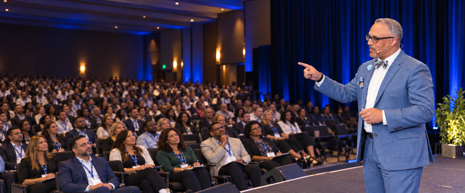 Larry Walters speaking in a blue suit on stage before a large corporate conference audience