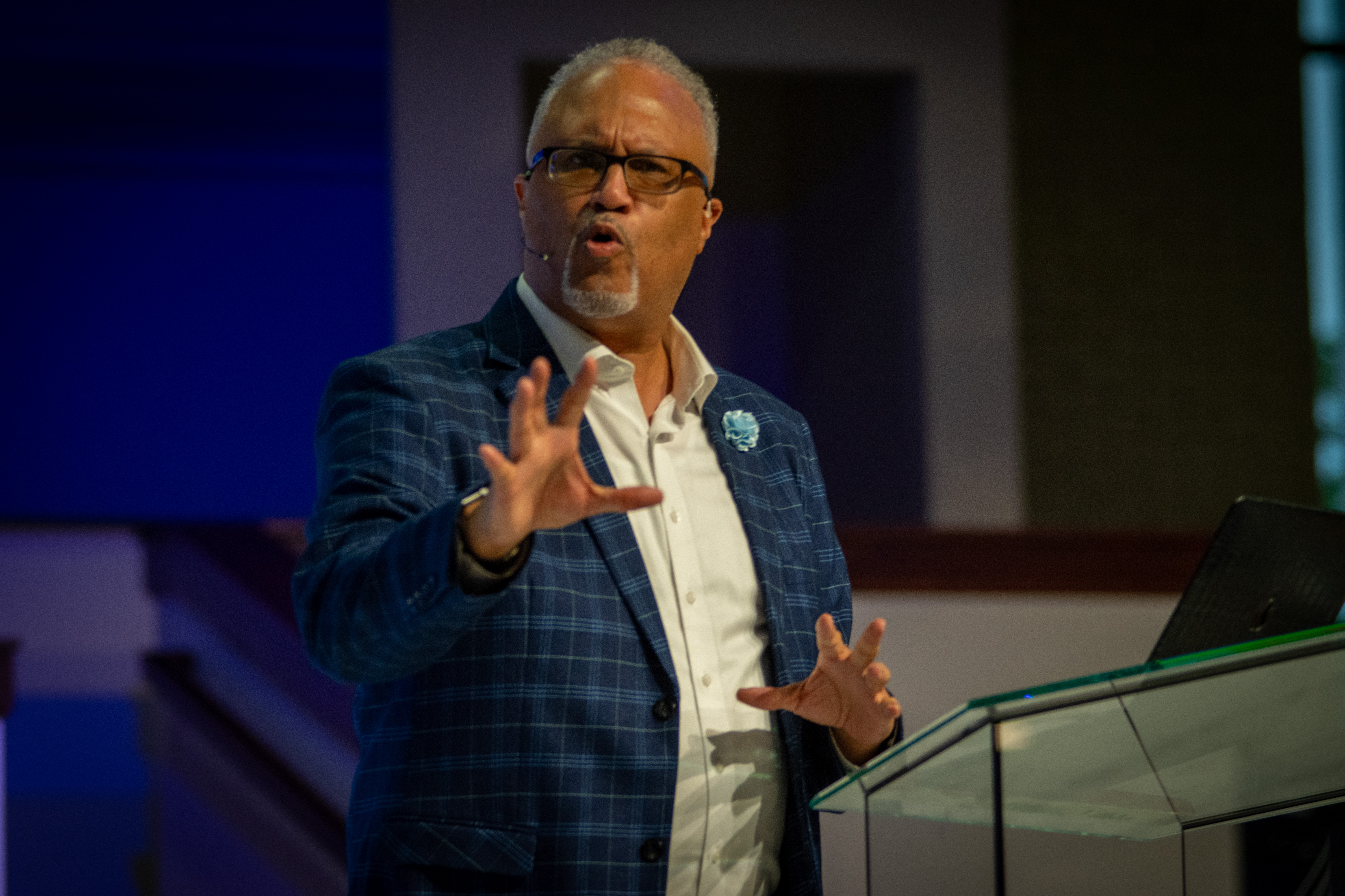 Larry Walters in a blue blazer addressing the audience, raising his hand to emphasize a point
