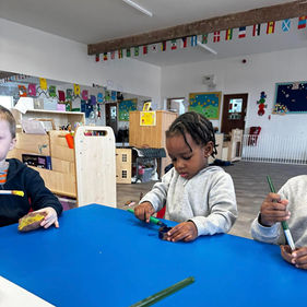 A young child sits at a blue table, focused on painting with a brush