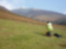 A person in a high-visibility jacket uses surveying equipment on a grassy hillside