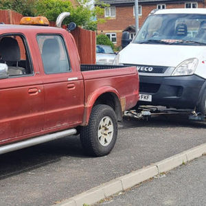 Red pickup truck towing a white flatbed truck on a suburban street