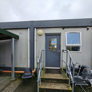 Light grey portacabin with a dark grey door and metal handrails on concrete steps