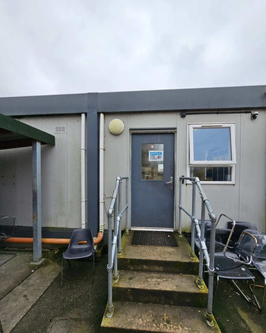 Light grey portacabin with a dark grey door and metal handrails on concrete steps