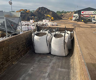 Four large bags filled with soil sit in the back of an industrial vehicle