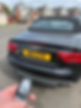A hand holding an Audi smart key fob in front of the rear tailgate of a black Audi S5 cabriolet with a fabric soft top