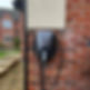 Electric vehicle charging station mounted on an exterior brick wall of a house, with a coiled cable