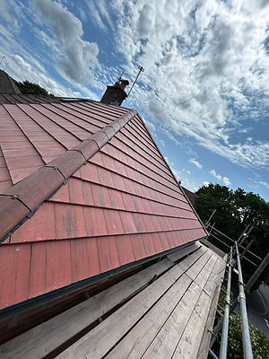 A red-tiled roof with a prominent ridge is shown against a partly cloudy sky.