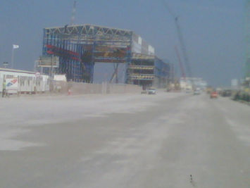 A wide shot from a dusty road leading towards a large blue steel industrial building under construction