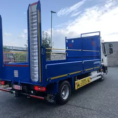 A blue flatbed truck with raised metal ramps is parked on a street