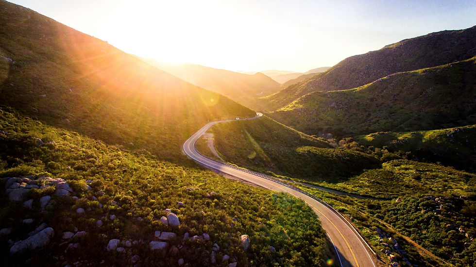 A winding road curves through sunlit green hills under a bright sunrise