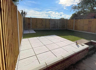 A small, sunny backyard with a square patio made of light-colored tiles