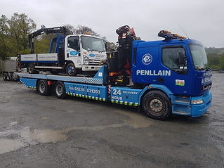 Blue tow truck labeled "Penllain" carries a smaller truck on a rainy day