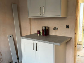 White kitchen cabinets with silver handles against an unfinished wall