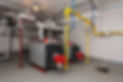 Two commercial boilers with red and gray casings are connected by yellow gas pipes