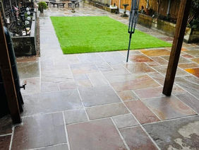 A spacious garden patio laid with wet, multi-toned Indian sandstone paving slabs