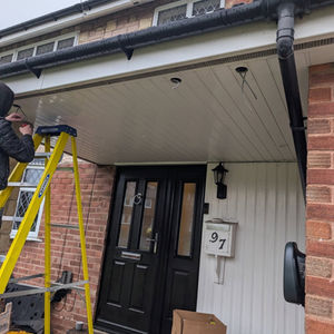 Person on yellow ladder installing lights under a white porch canopy of a brick house